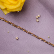 A sterling silver bracelet with a braided pattern displayed on a purple fabric surface, accompanied by small golden beads and a yellow flower.
